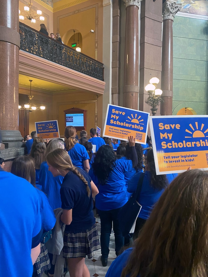 A group of students and parents wearing blue shirts and holding protest signs in support of the Illinois tax-credit scholarship rally inside the Illinois State Capitol building.