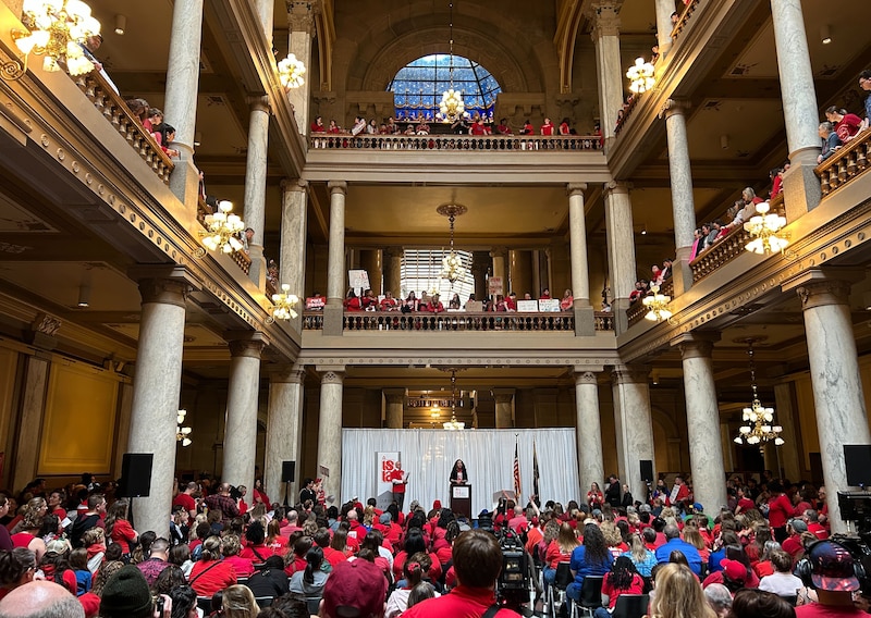 A large group of people in red t-shirts gather in a large state Capitol building.