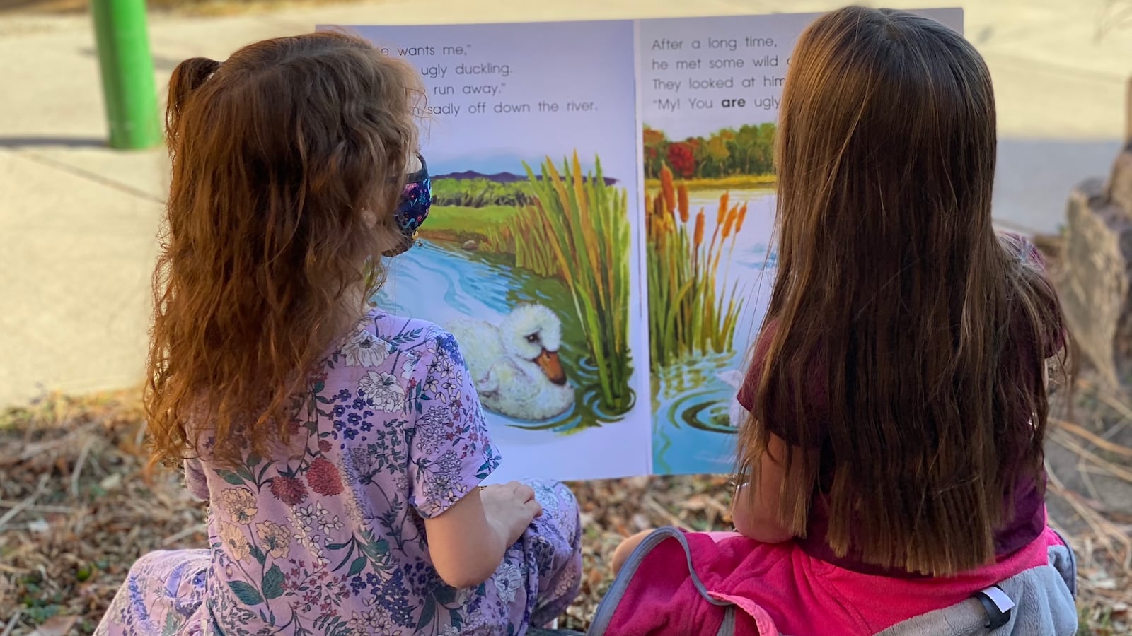 Two first grade girls read a large book outside.