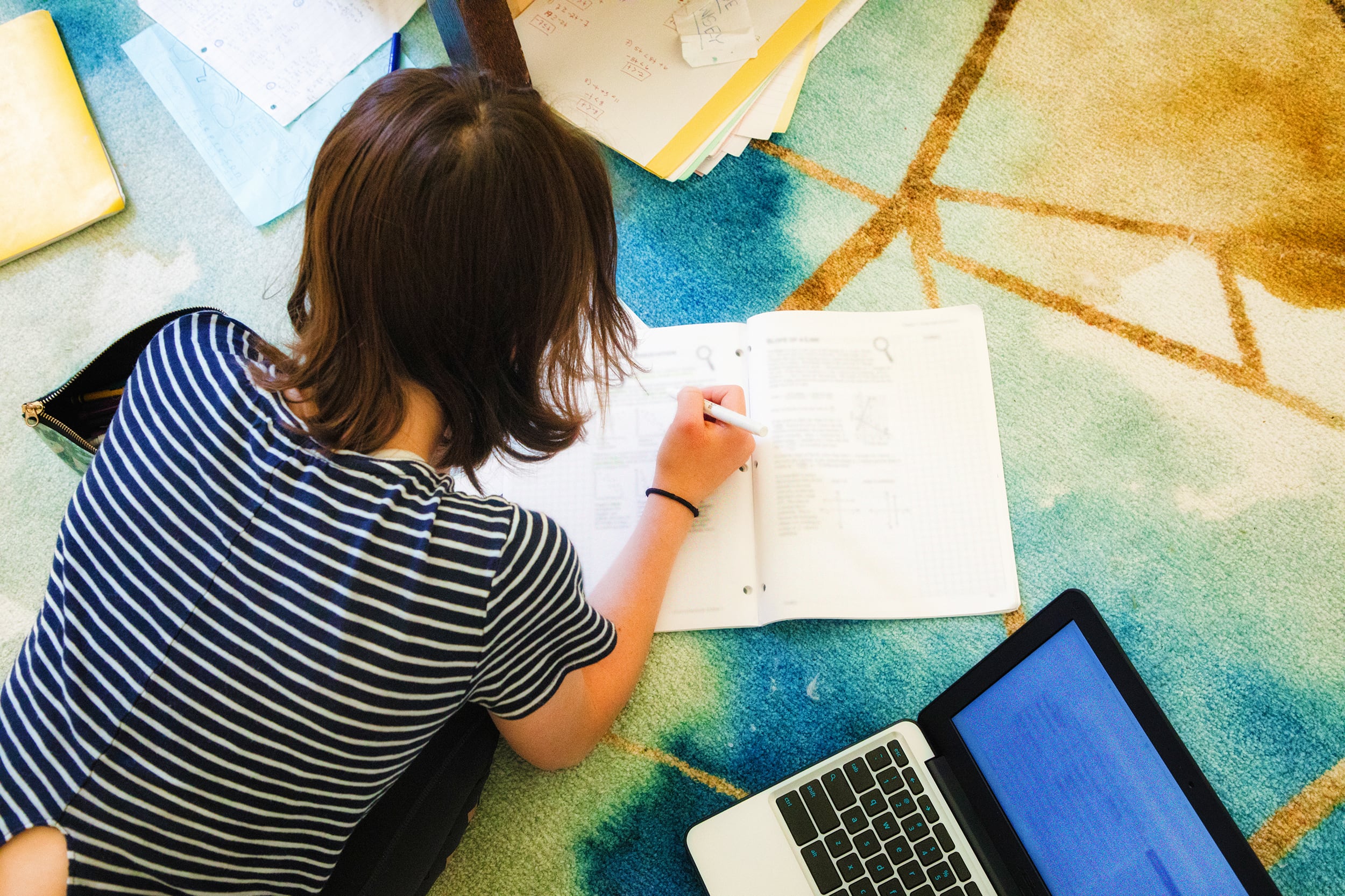 Overhead view of teenage female doing her homework on the carpet with laptop