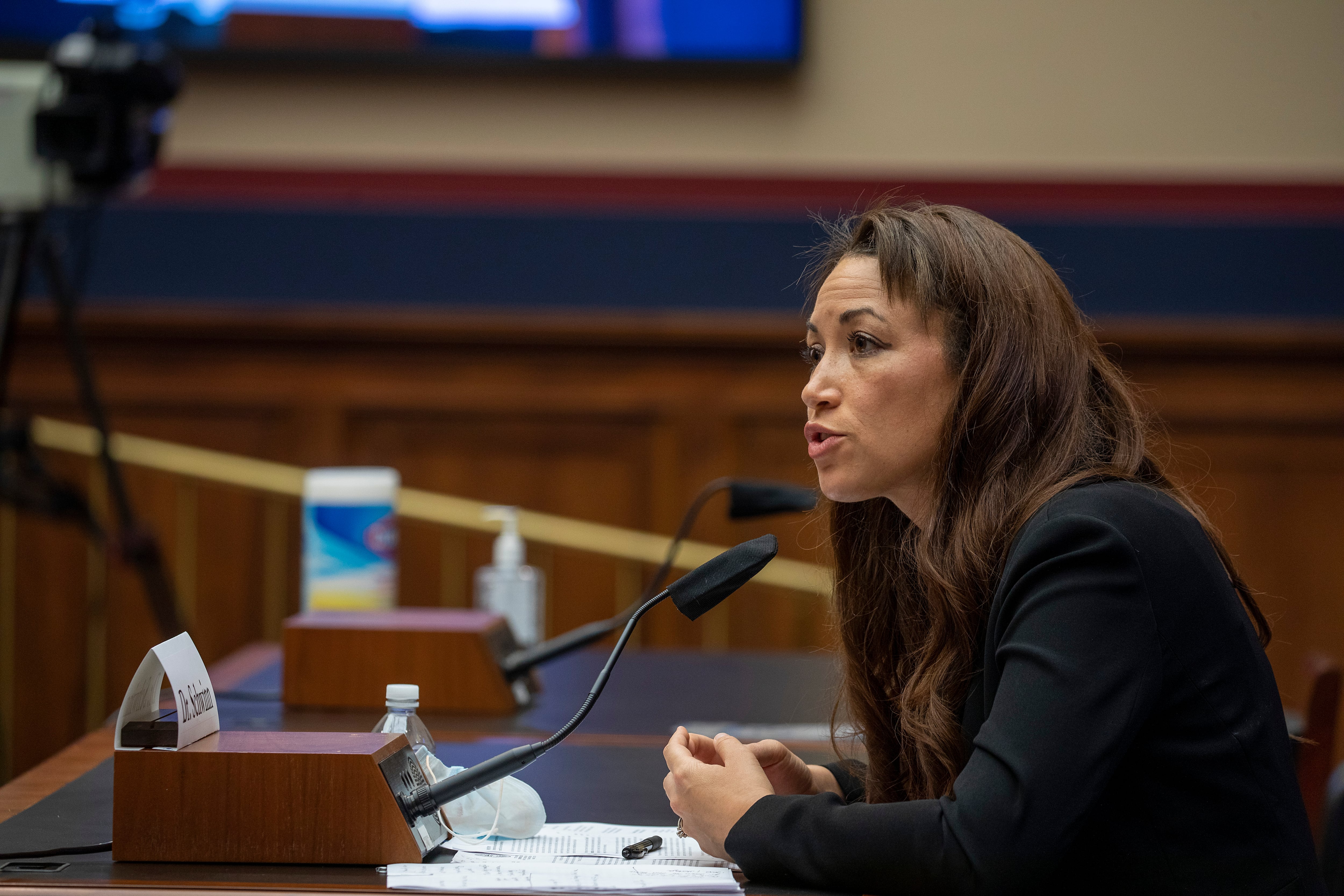 A woman in a dark suit jacket speaks into a microphone.