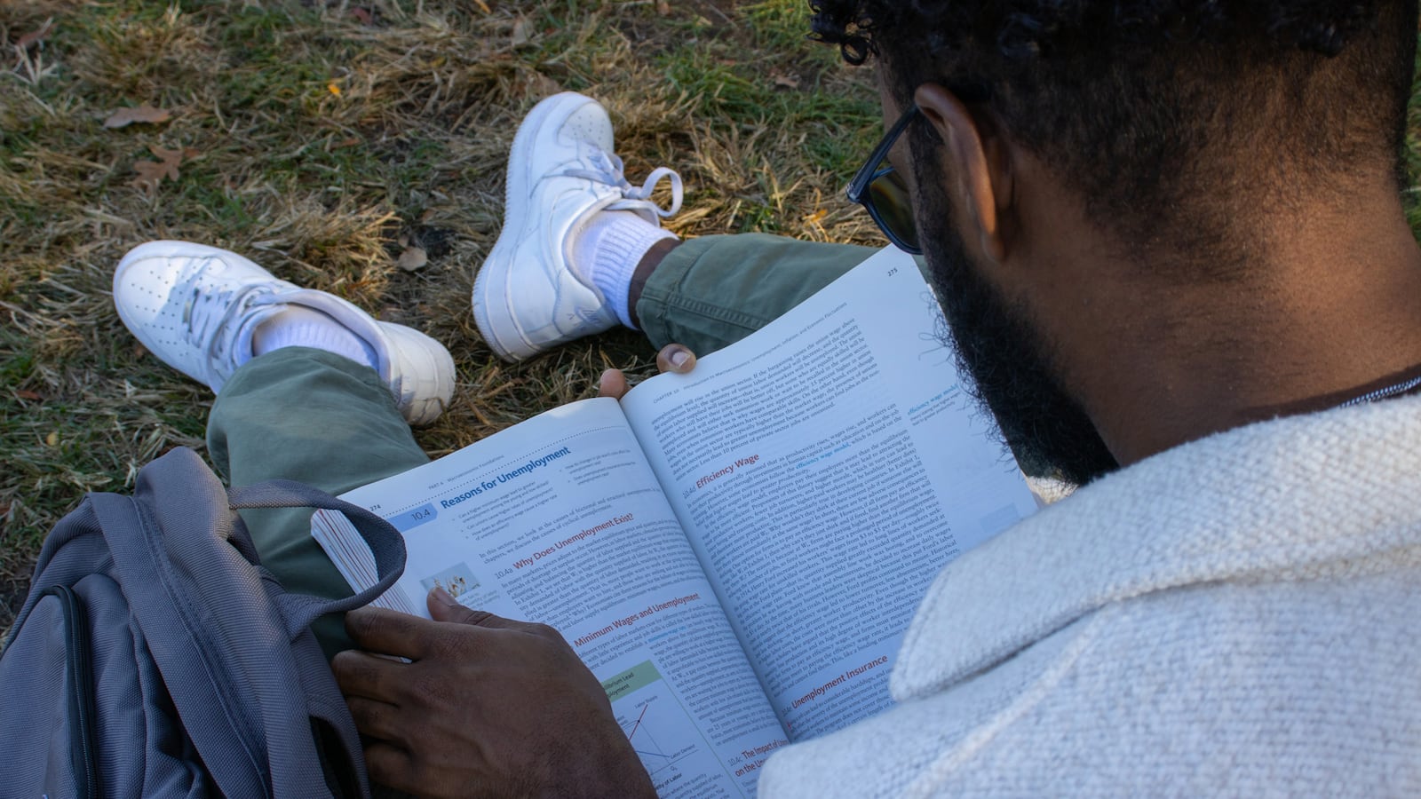 A person reads a textbook outside sitting on the grass.