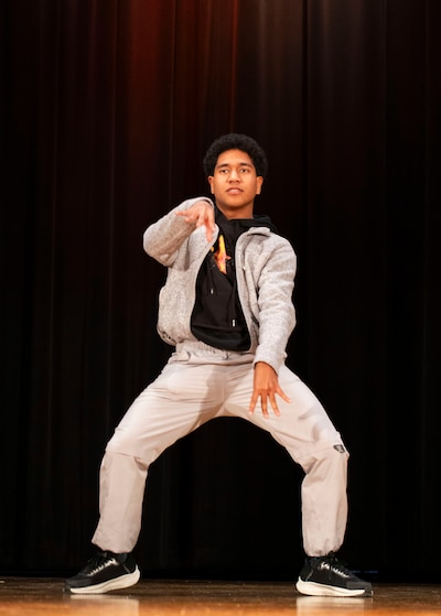 A photograph of a Black high school student dancing on a stage.