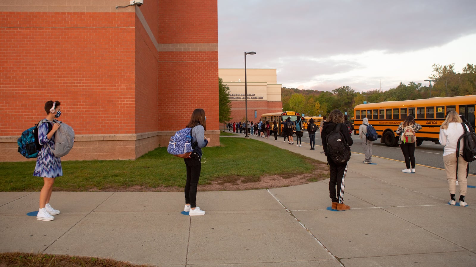Students line up on socially distanced dots painted on the sidewalk to wait their turn to be scanned by a temperature screener before classes at Middletown High School.