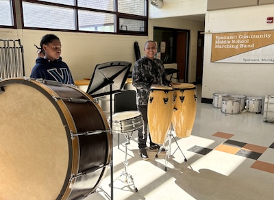 Two middle school students stand behind drums in a music classroom.
