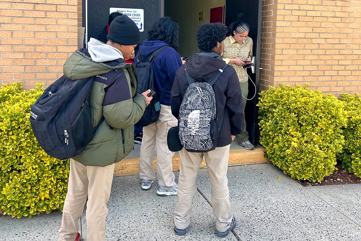 students with backpacks gathered outside a brick building.
