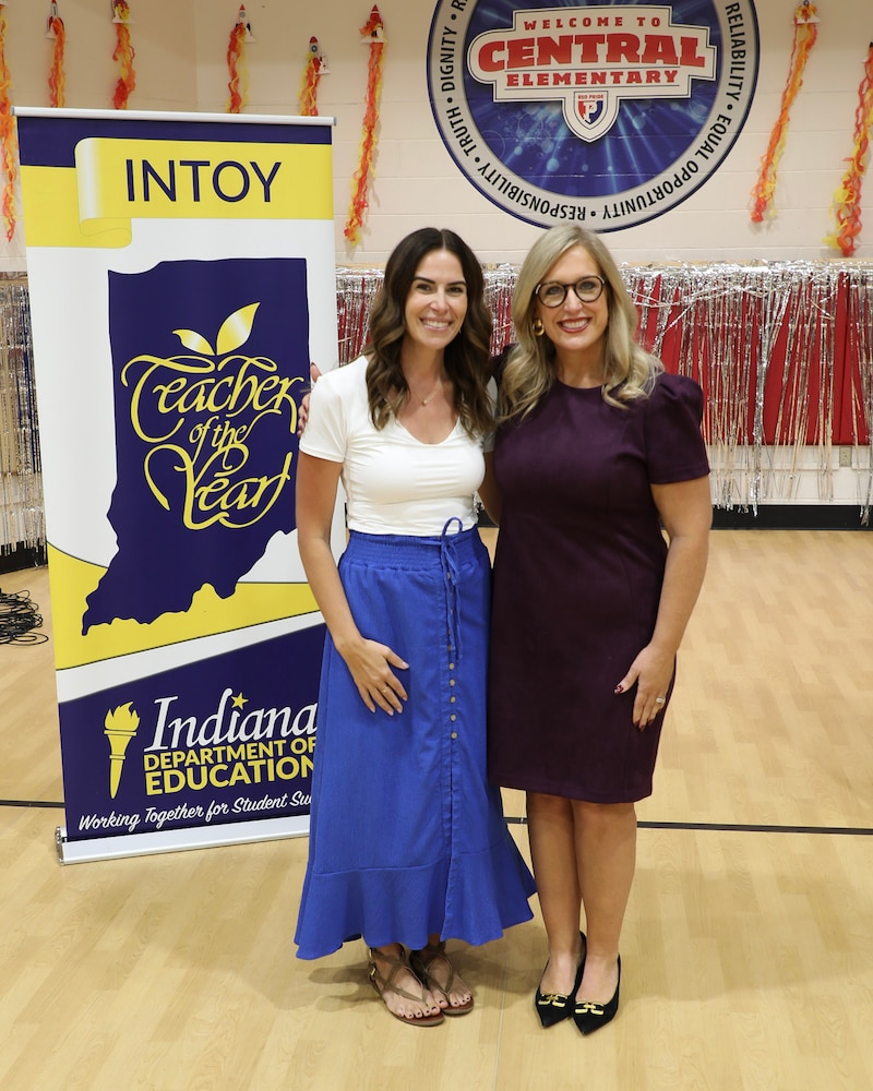 A photograph of two white women standing next to each other posing for a portrait in a school gym.