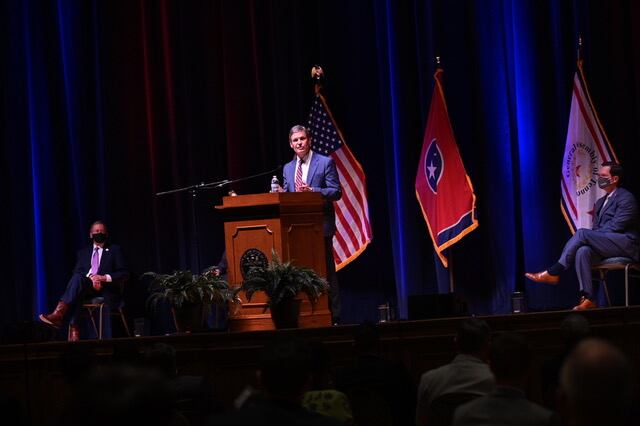 Gov. Bill Lee stands on stage behind a podium in front of an American and Tennessee flag. State legislators are spaced out in the audience to social distance.