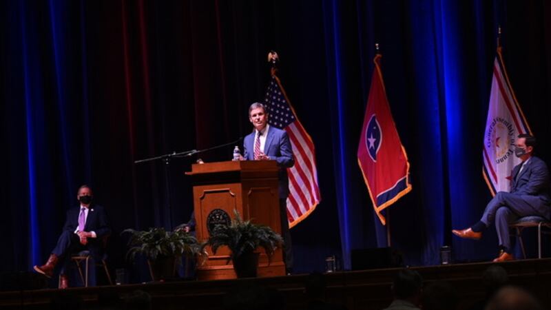 Gov. Bill Lee stands on stage behind a podium in front of an American and Tennessee flag. State legislators are spaced out in the audience to social distance.