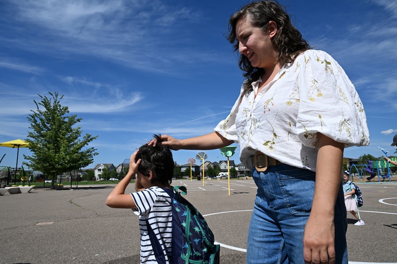 An adult woman holds the hand of a young boy outside.