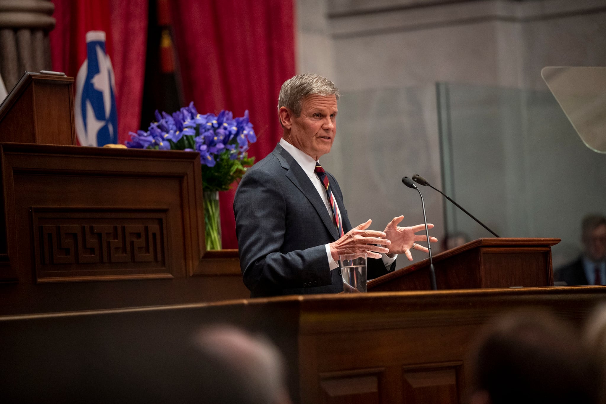 A man wearing a suit stands at a podium and speaks into a microphone.