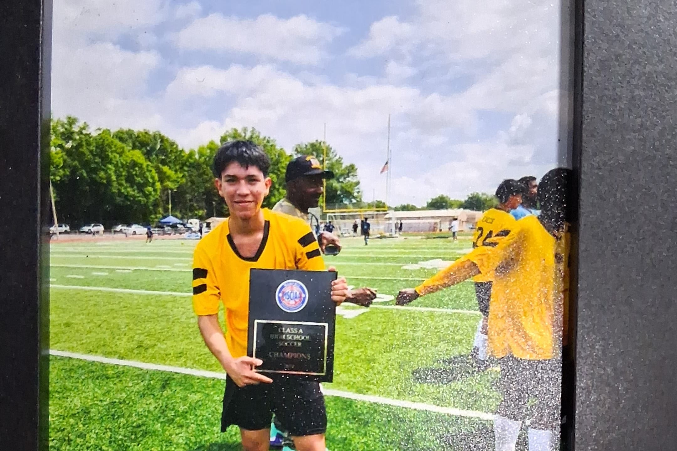 Yasser Jose Lopez Soza, 18, stands on a soccer field in a framed photograph. He's holding a black plaque and wearing a bright yellow uniform.