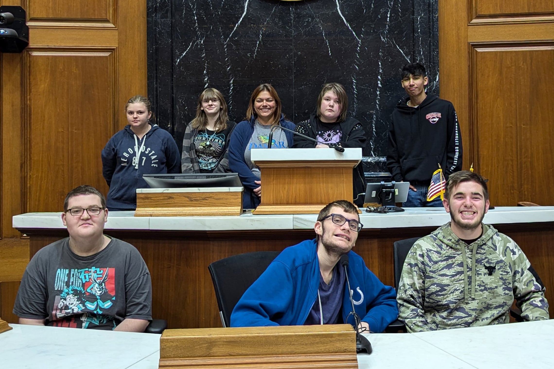 Three male students in the foreground and four other students and a female teacher visit the legislature.