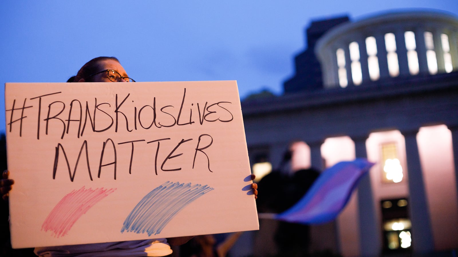 A person holds a sign that says #TransKidsLivesMatter.