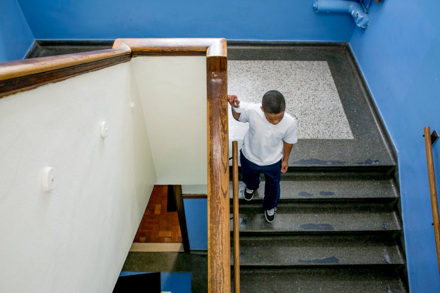 A young student wearing a blue shirt walks down a school stairway.