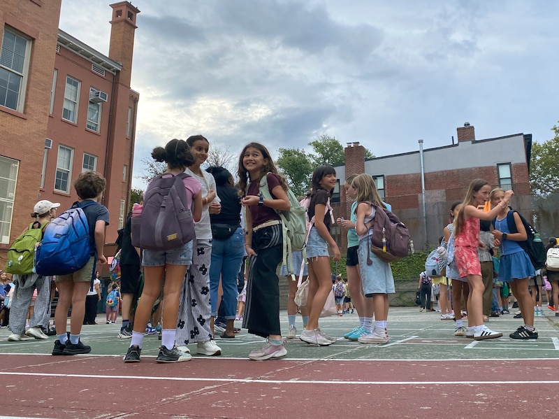 Students wait outside of a school building on a playground on a cloudy day.