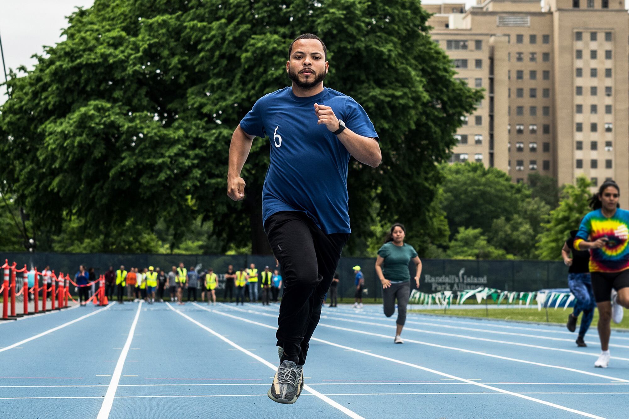 A man in a blue T-shirt and black pant running on a track.