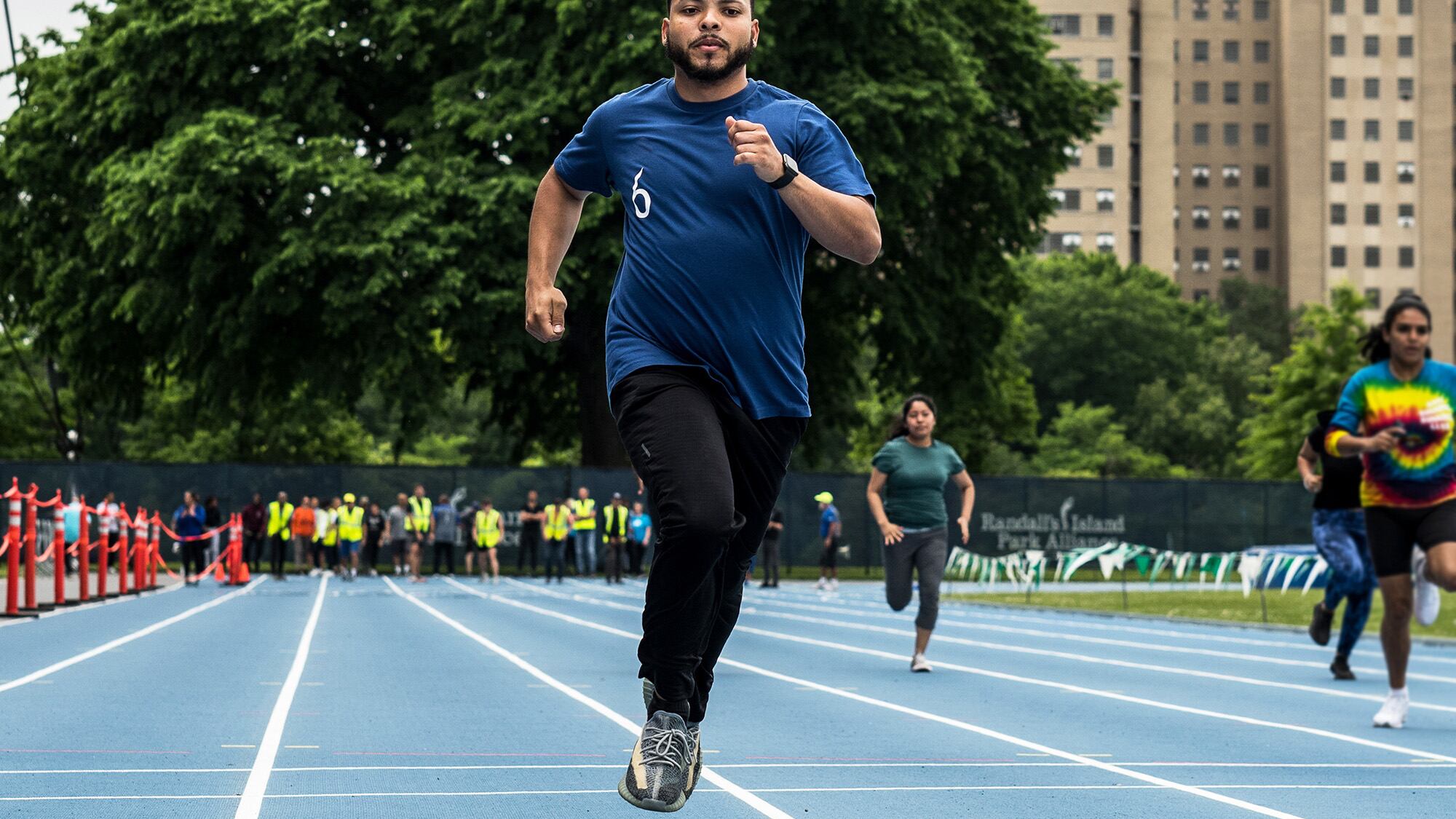 A man in a blue T-shirt and black pant running on a track.