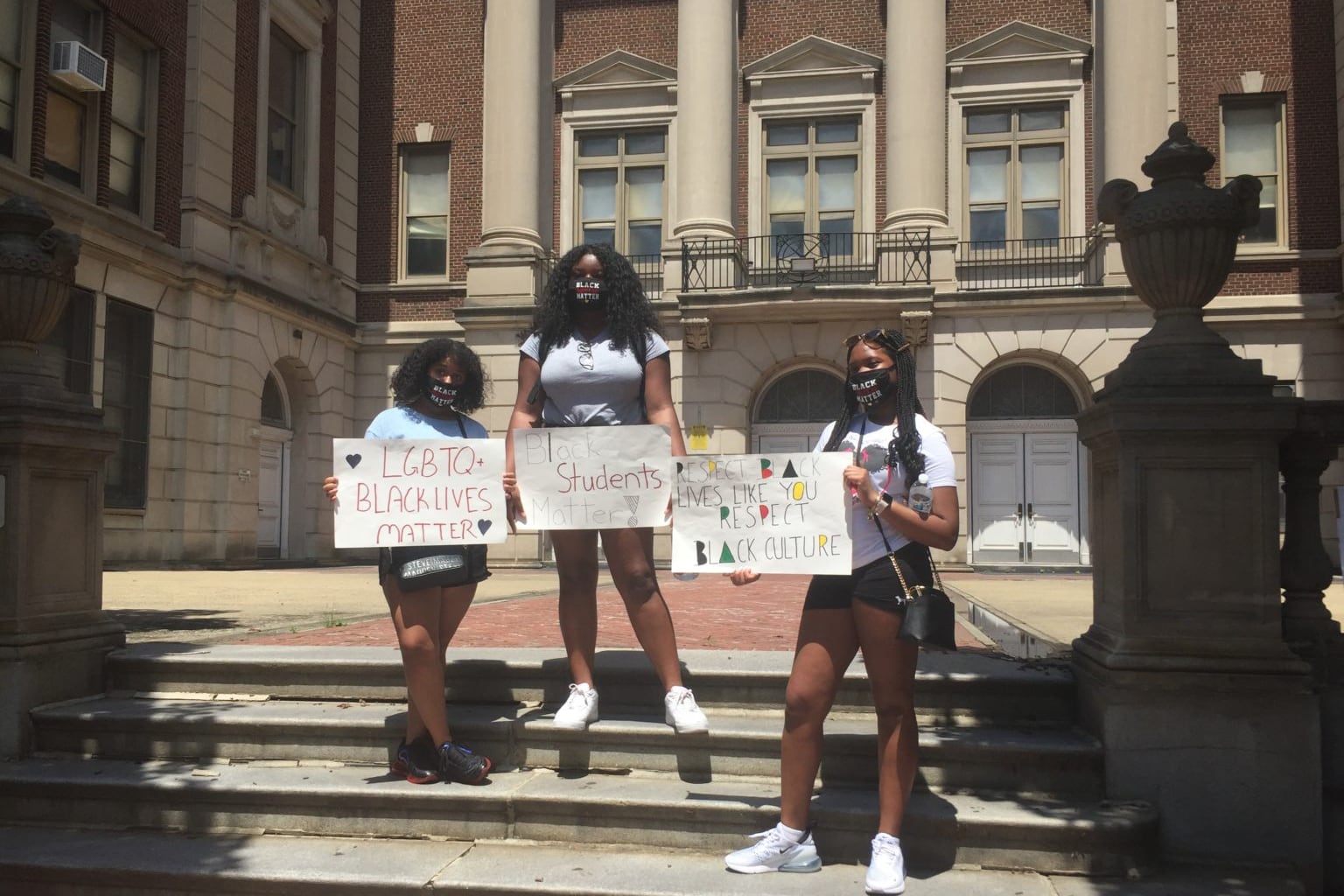 Students holding protest signs stand on the steps outside Julia R. Masterman Laboratory and Demonstration School,