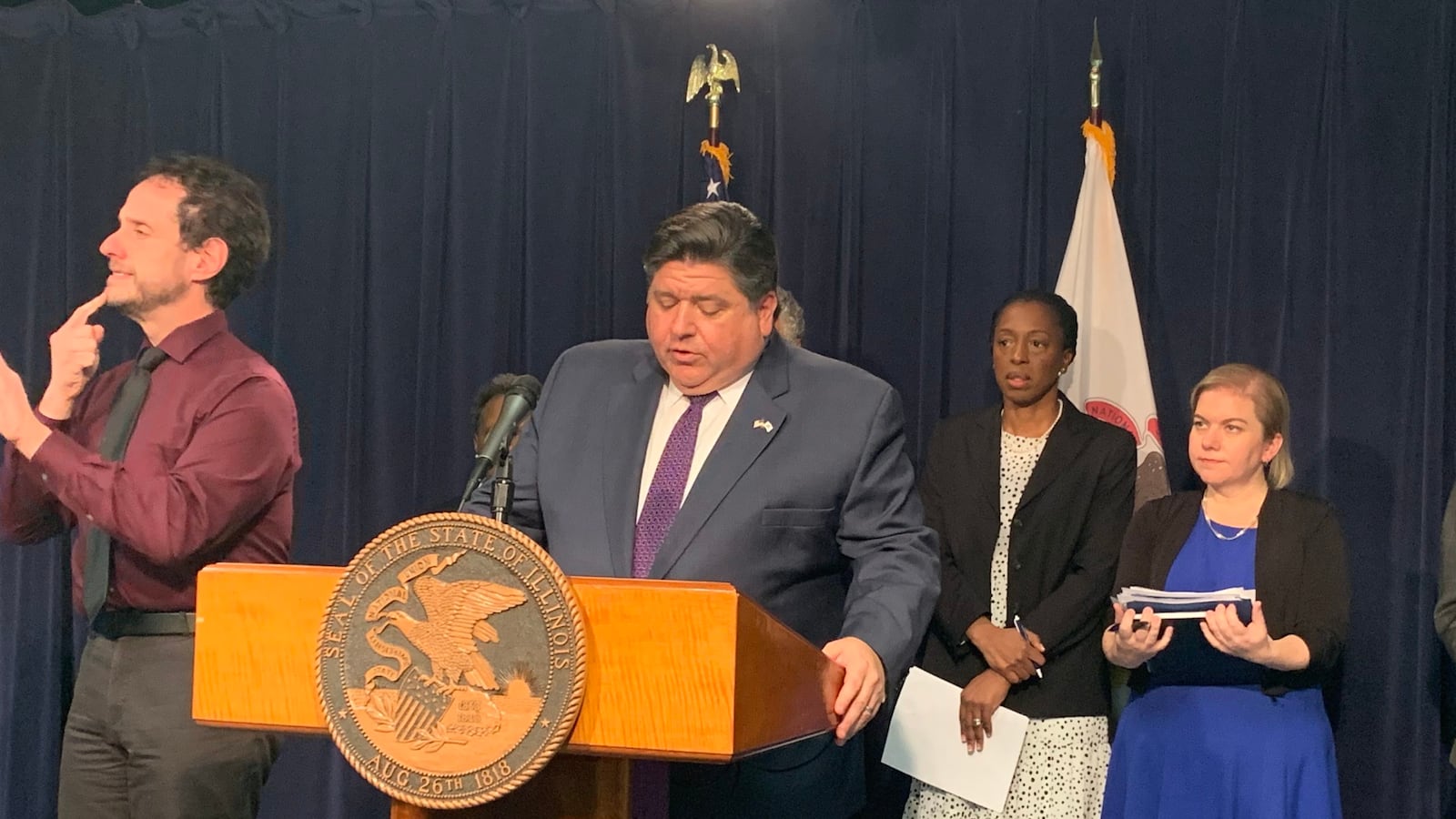 Illinois Gov. J.B. Pritzker talks Thursday about measures to counter the spread of the novel coronavirus. He is flanked on the left by an interpreter and on the right by Illinois public health Director Ngozi Ezike and Chicago public health Commissioner Allison Arwady.