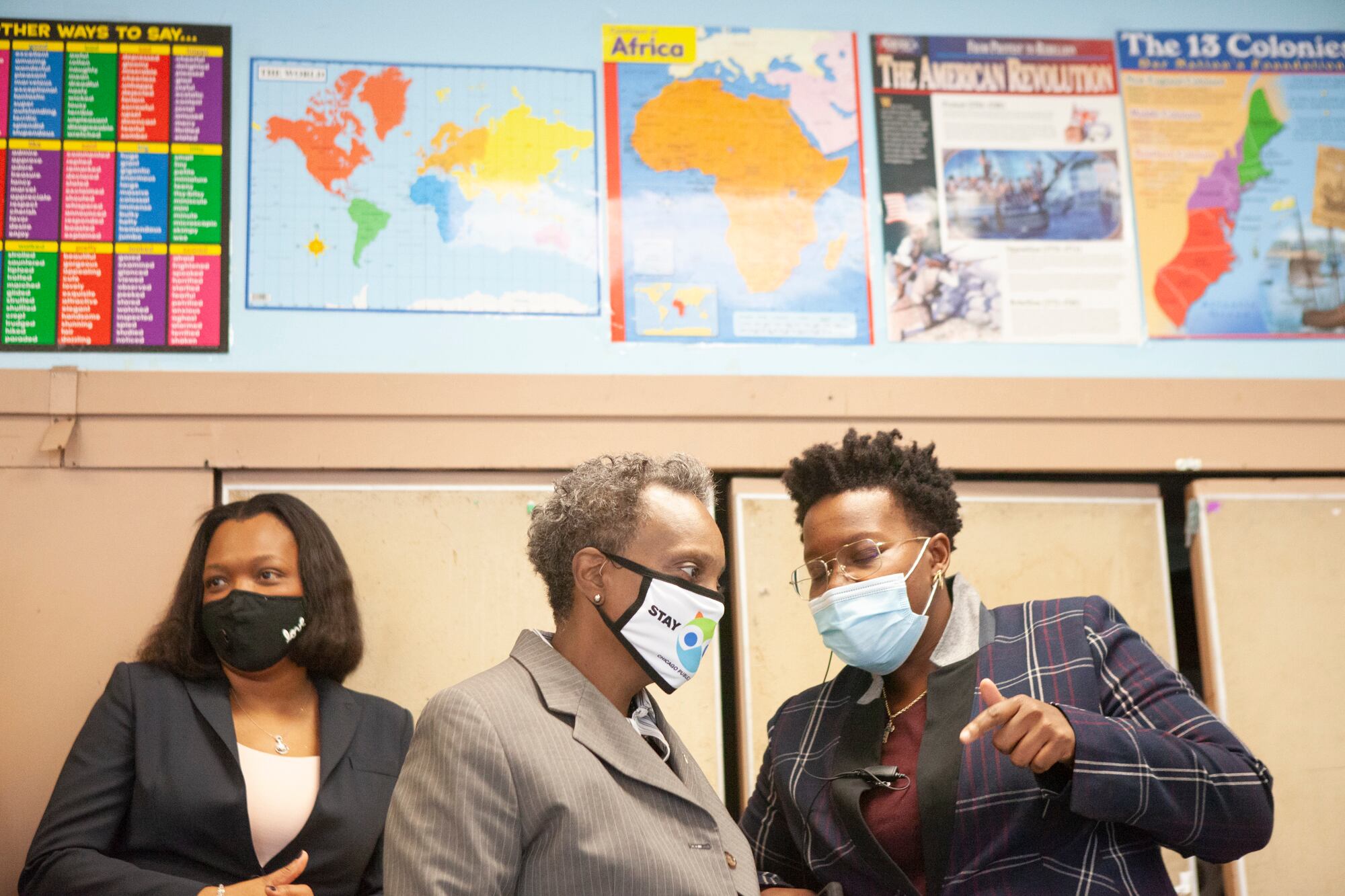 All wearing masks, Mayor Lori Lightfoot talks with Principal Jasmine Thurmond and standing next to school chief Janice Jackson, with maps on the wall behind them.