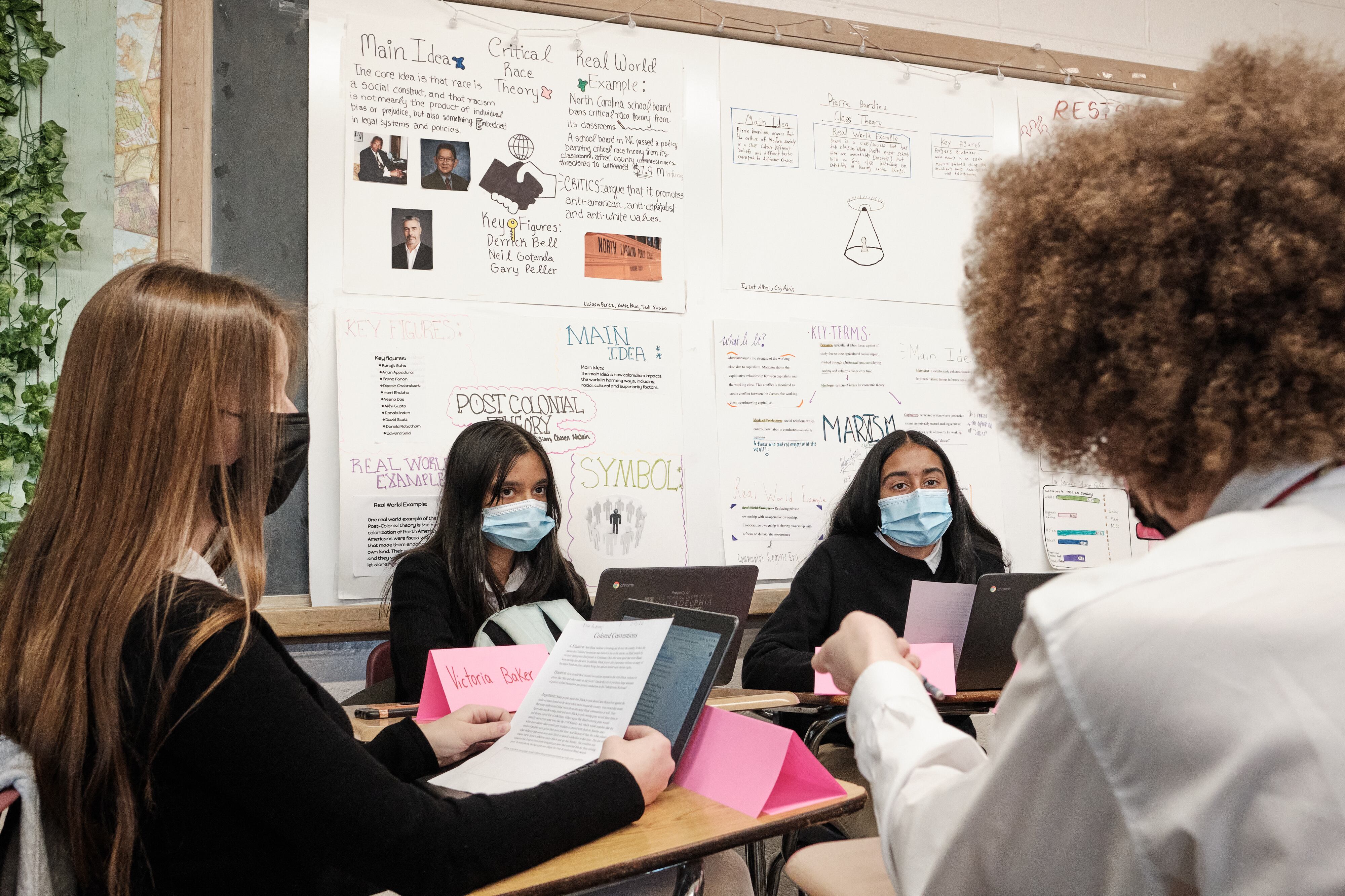Students work in small groups at their desks while wearing masks during a class on Black history.