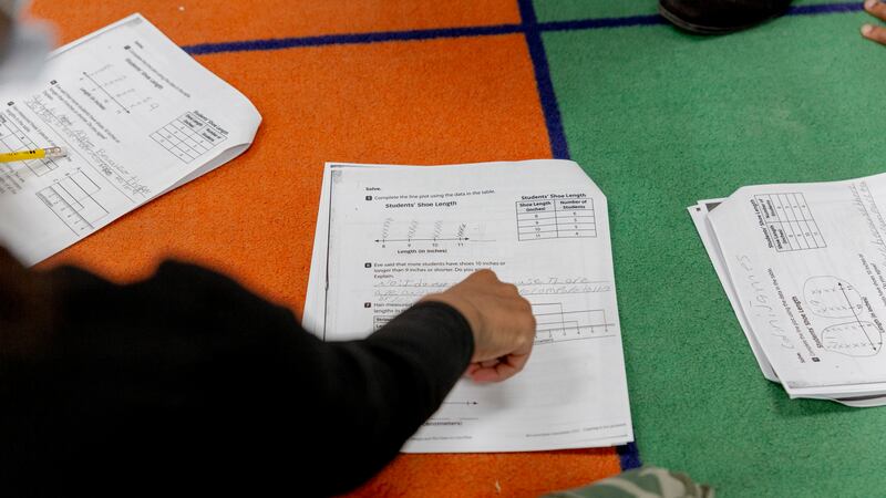 A person wearing a dark shit gestures with a hand towards a worksheet. 