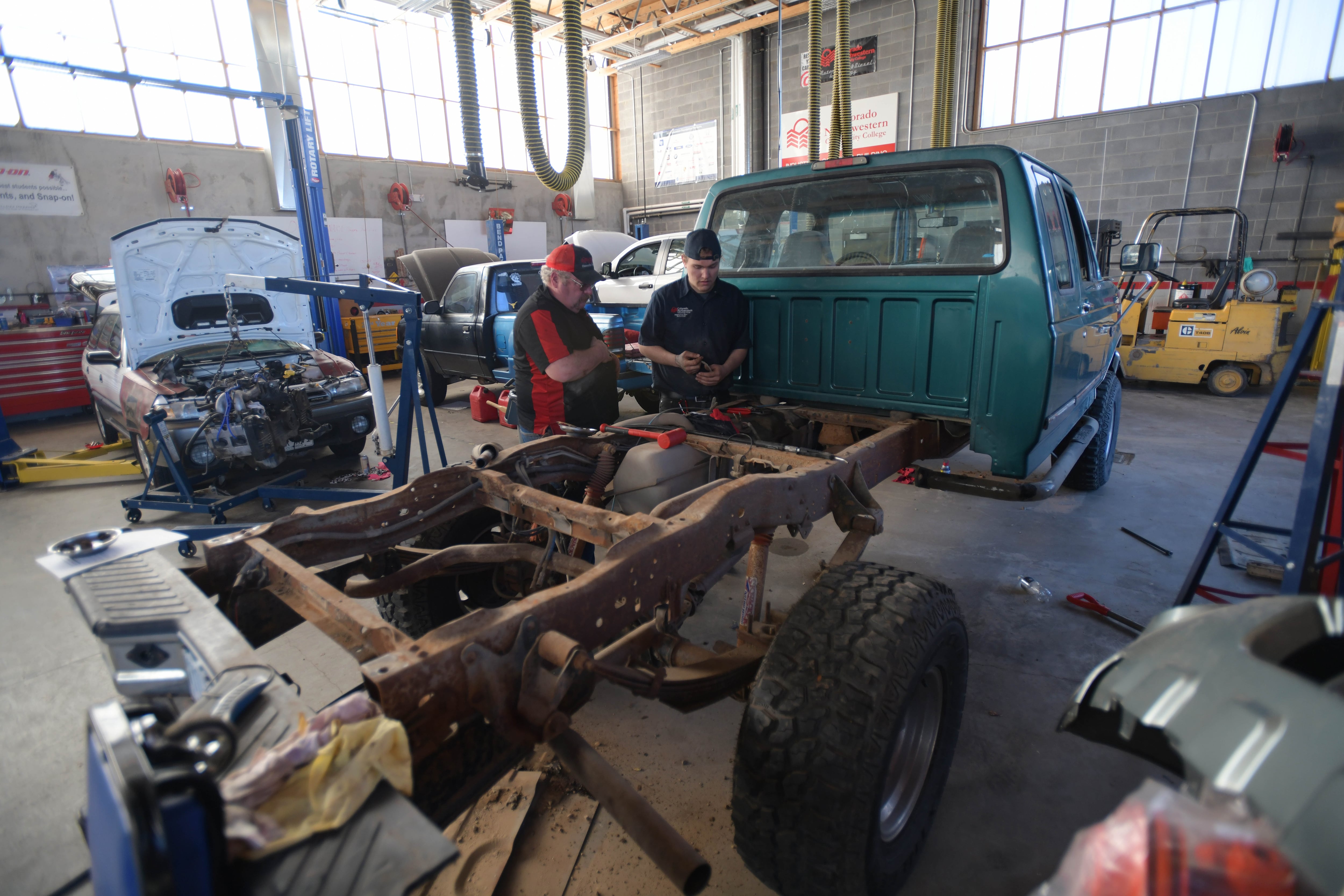 Two people stand in an automotive garage next to a truck needing repairs.