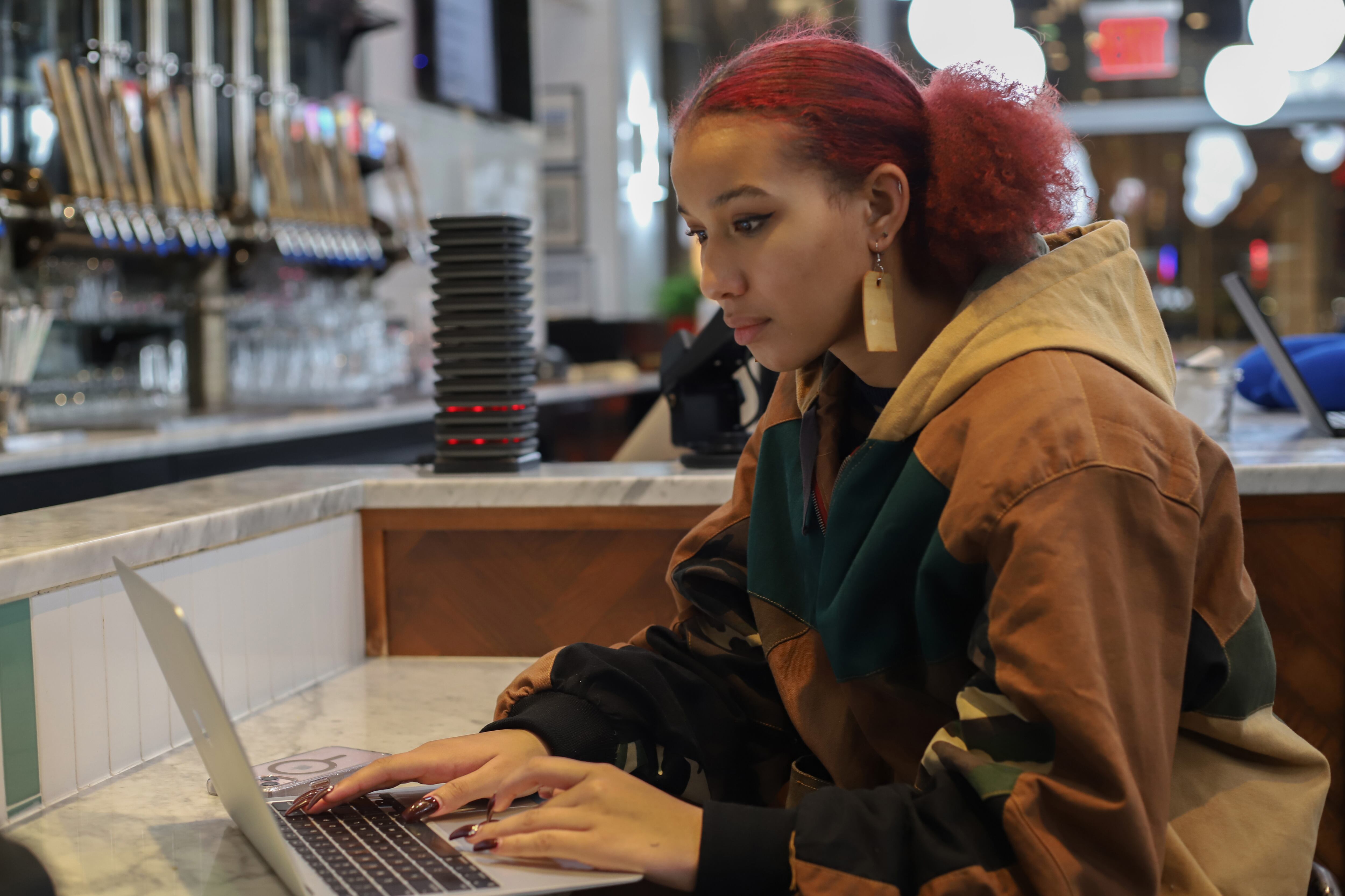 A student in a brown jacket sits at a table with an open laptop.