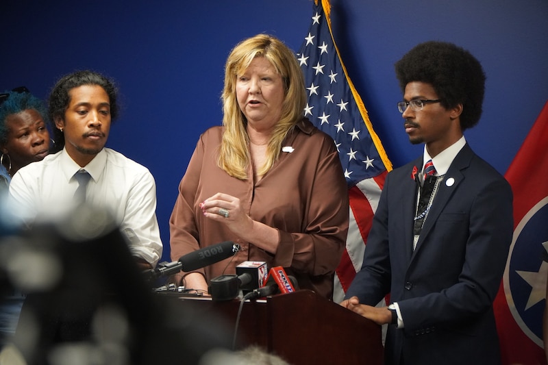 From left to right, a man, a woman and another man standing at a podium in front of U.S. and Tennessee flags.