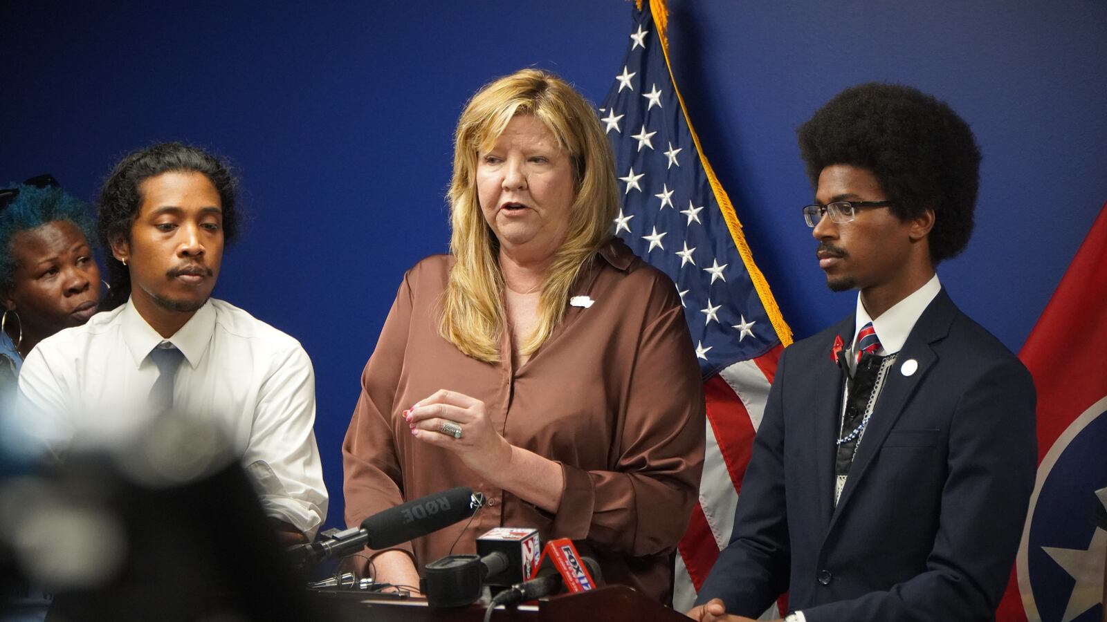 From left to right, a man, a woman and another man standing at a podium in front of U.S. and Tennessee flags.