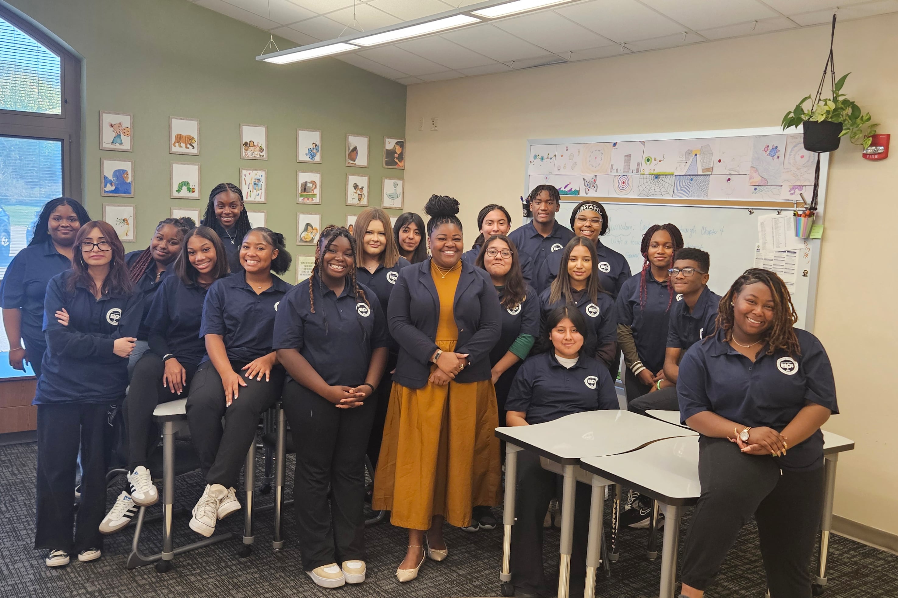 A group of students and a teacher pose for a portrait in matching shirts in a classroom.