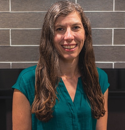 Headshot of a woman with long hair. She wears a teal short-sleeve shirt.