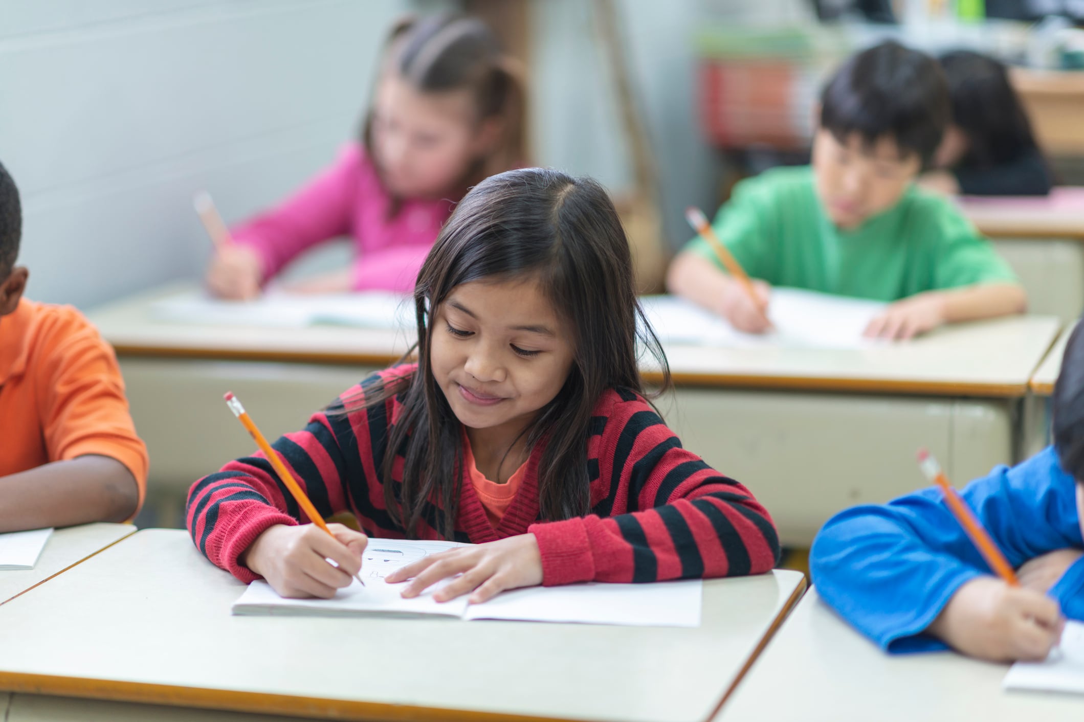 A girl in a red-and-black striped sweater sits at a desk with a pencil and paper.