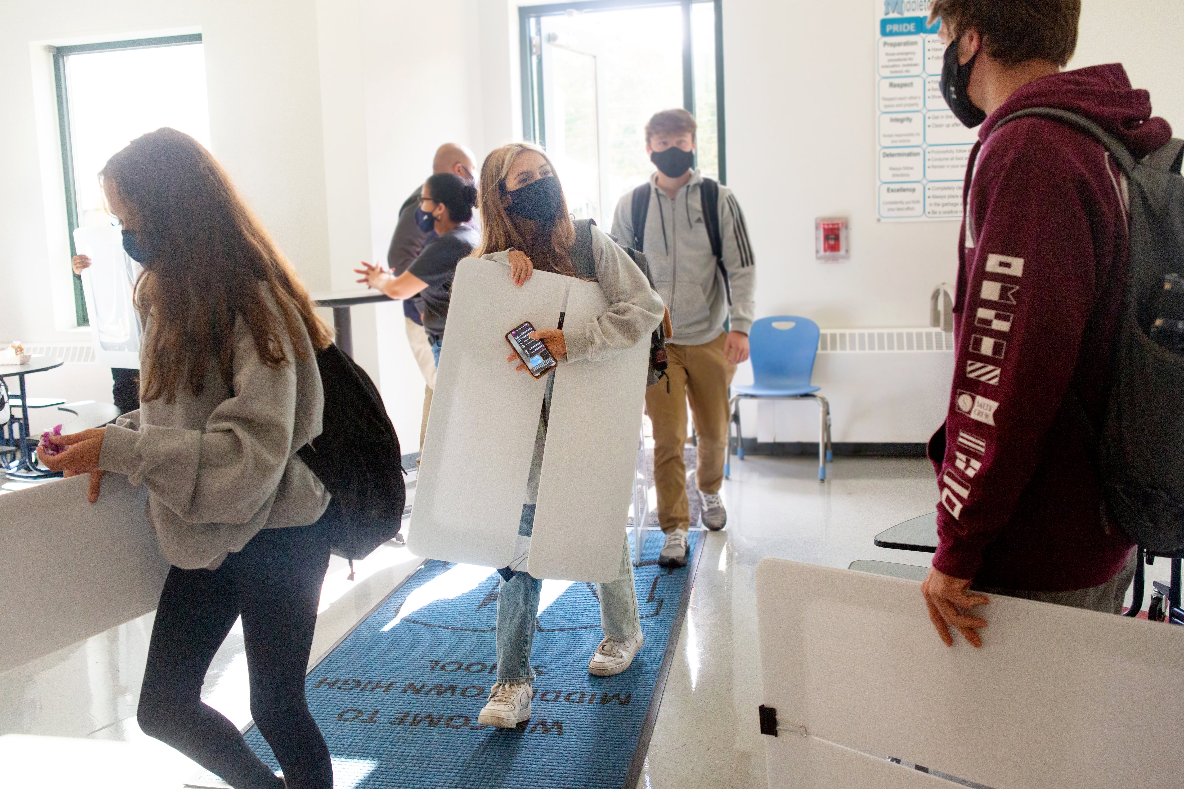 Students wearing face masks and carrying protective desk shields.