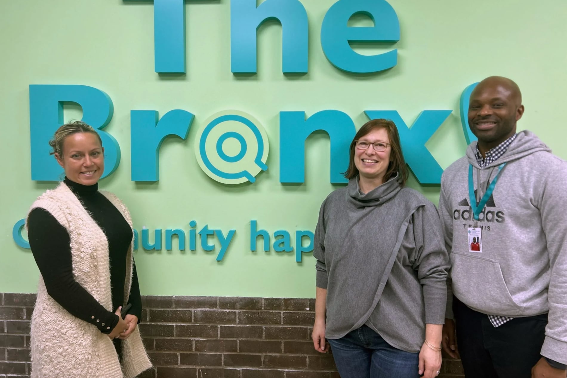 Three people stand in front of a green wall panel that says "Bronx."
