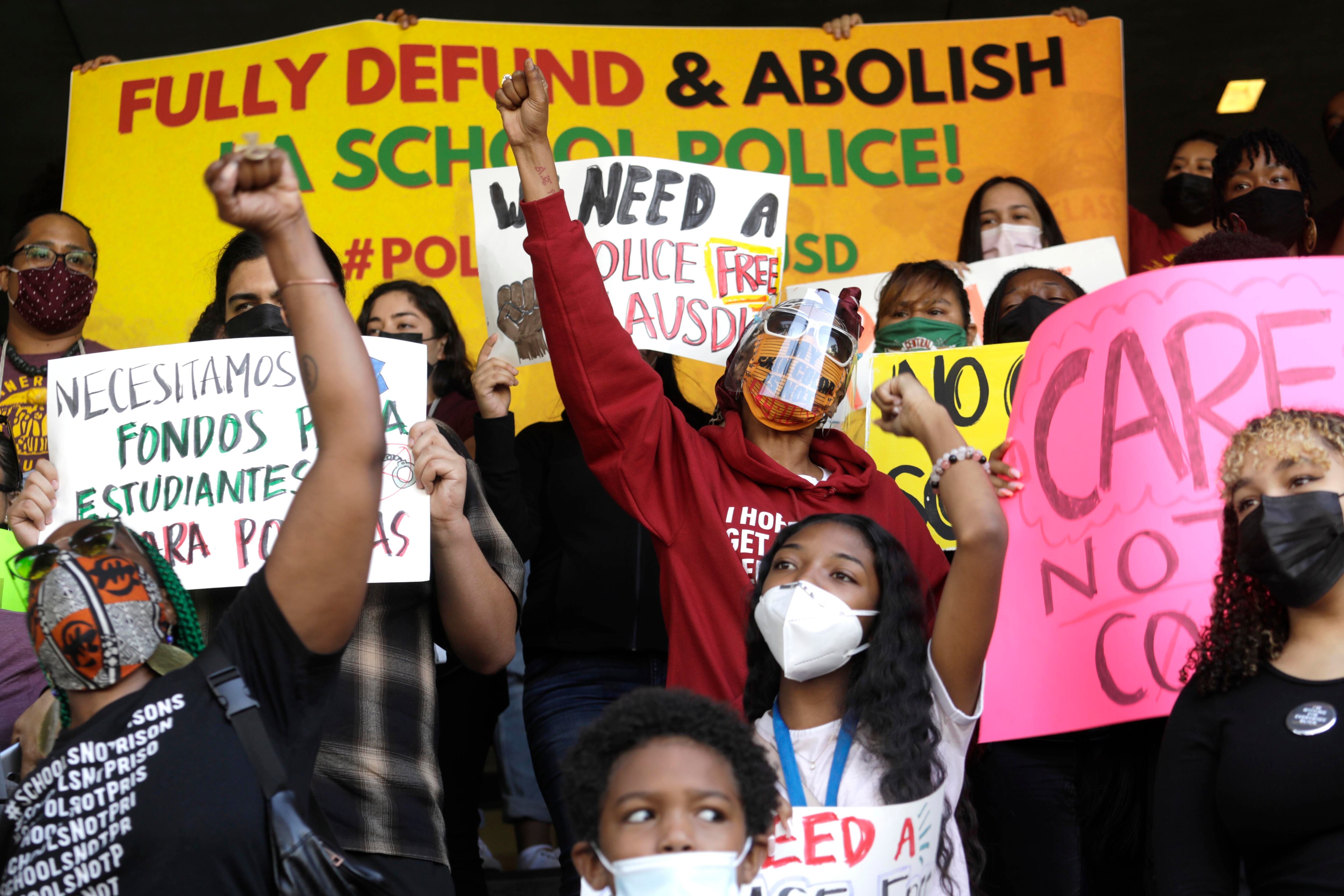 Several protestors wearing protective masks protest the presence of police in schools. A large yellow sign behind them reads “FULLY DEFUND & ABOLISH LA SCHOOL POLICE!”