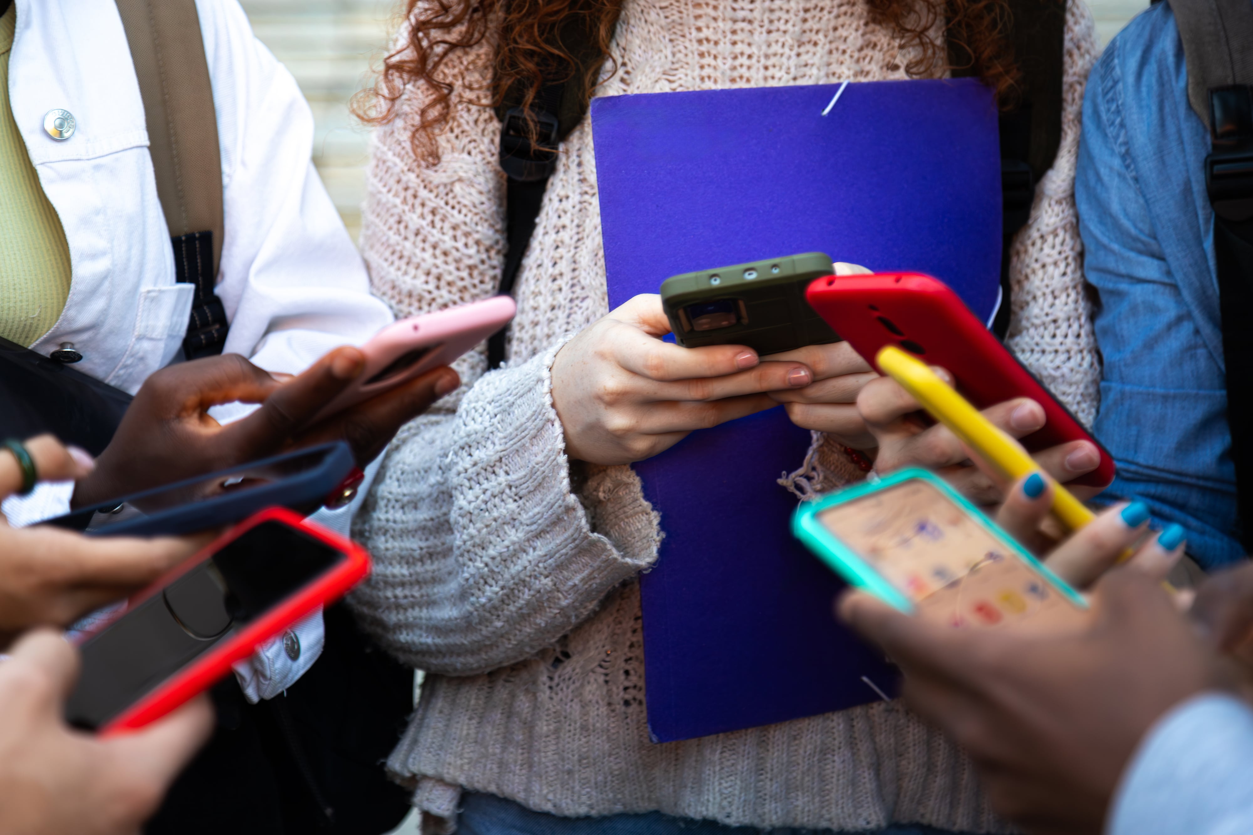 Close-up of young students' hands holding mobile phones.
