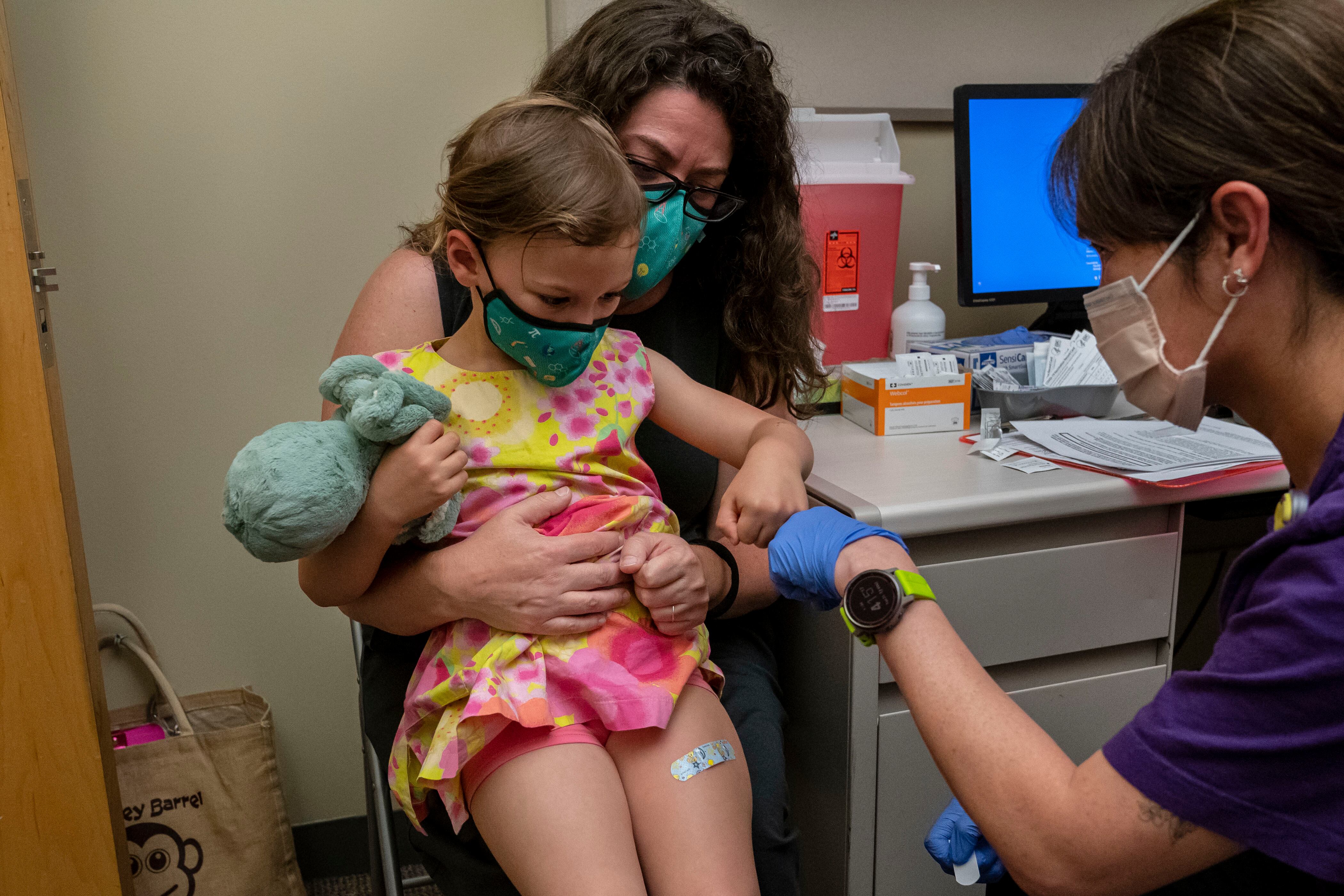 A young child being held by her mother receives a vaccine from a health care professional.