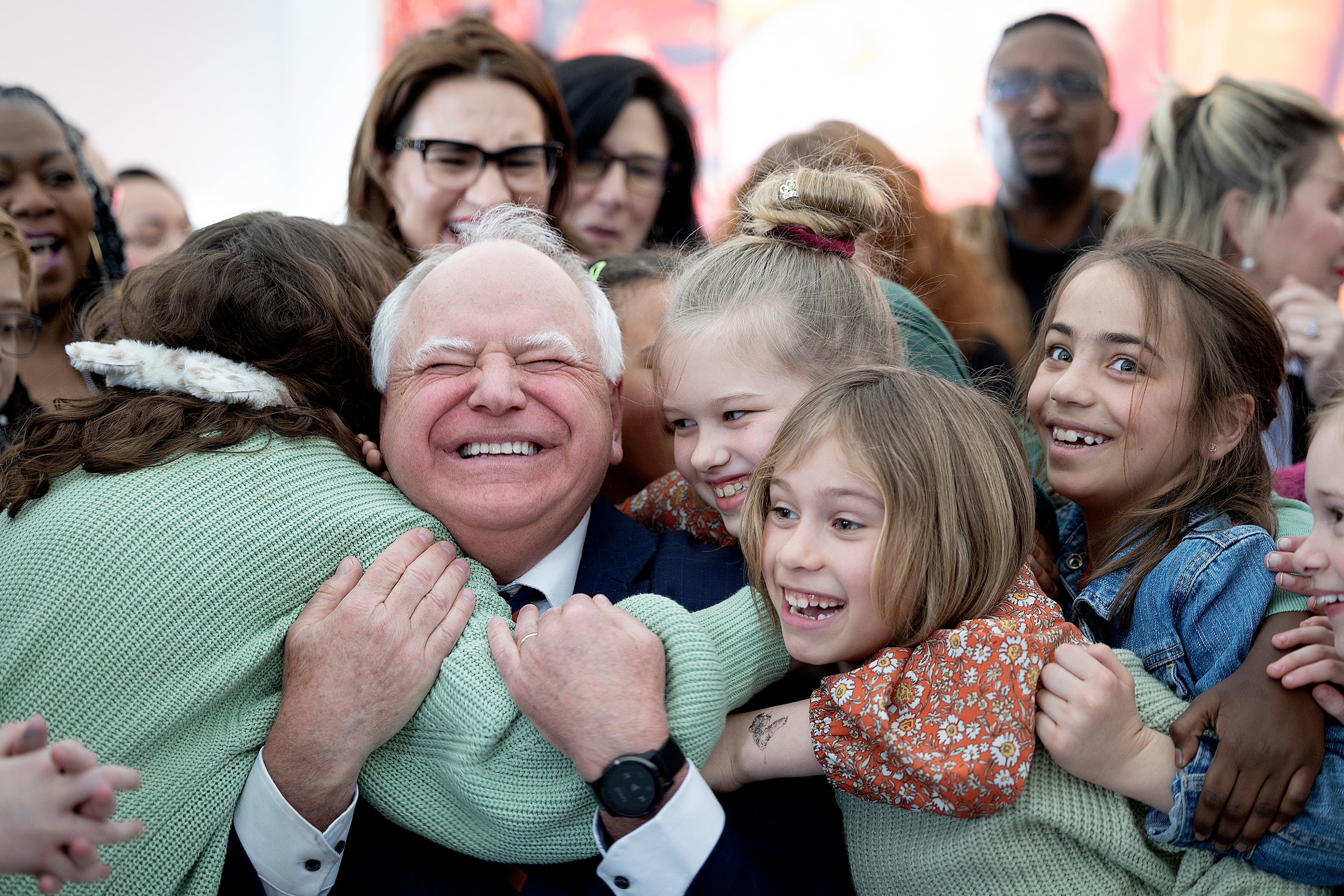 A group of young students give a group hug to an adult man who has his eyes closed and a giant smile.