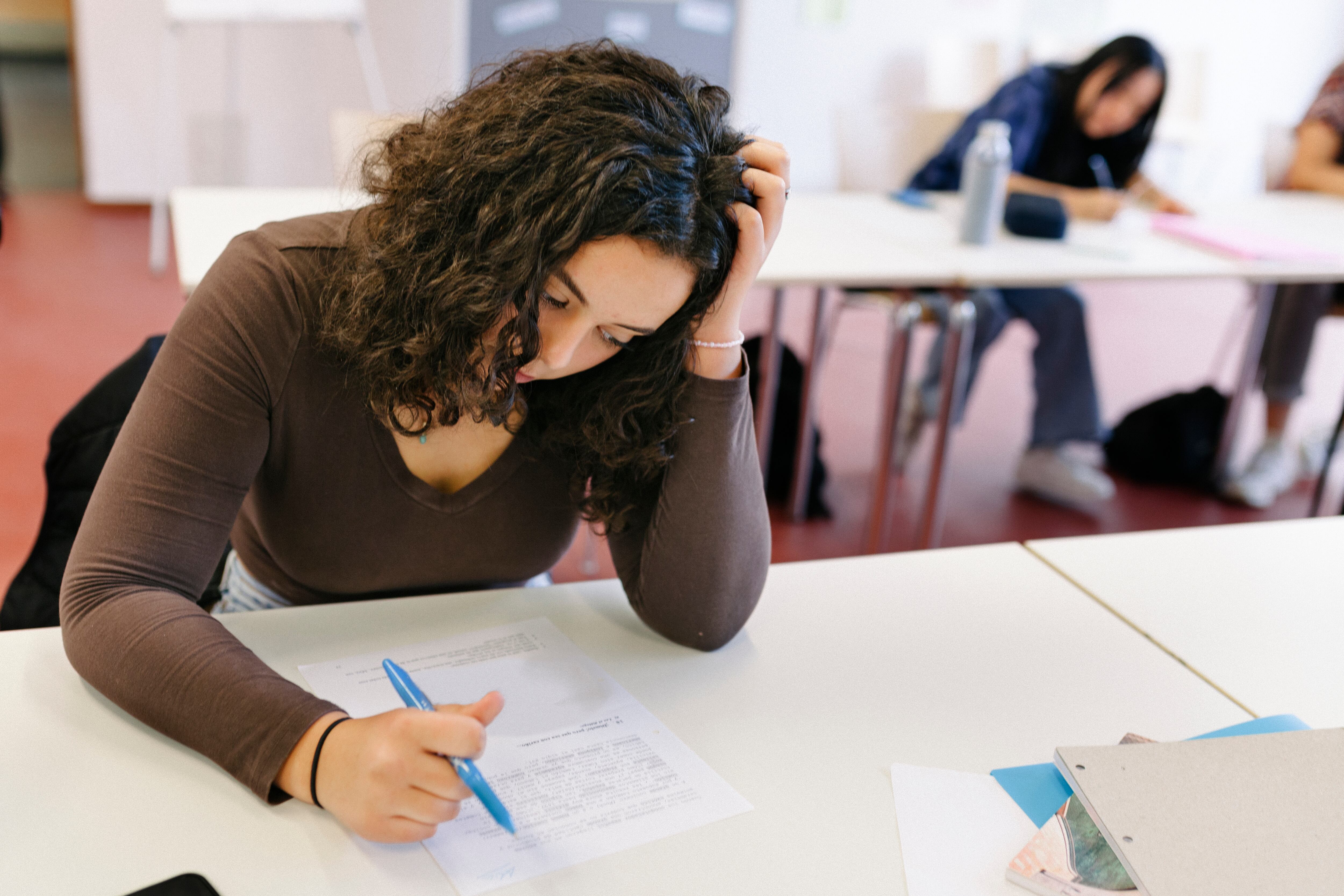 A person holds a pen in her right hand while seated at a desk and puts her head in her left hand.