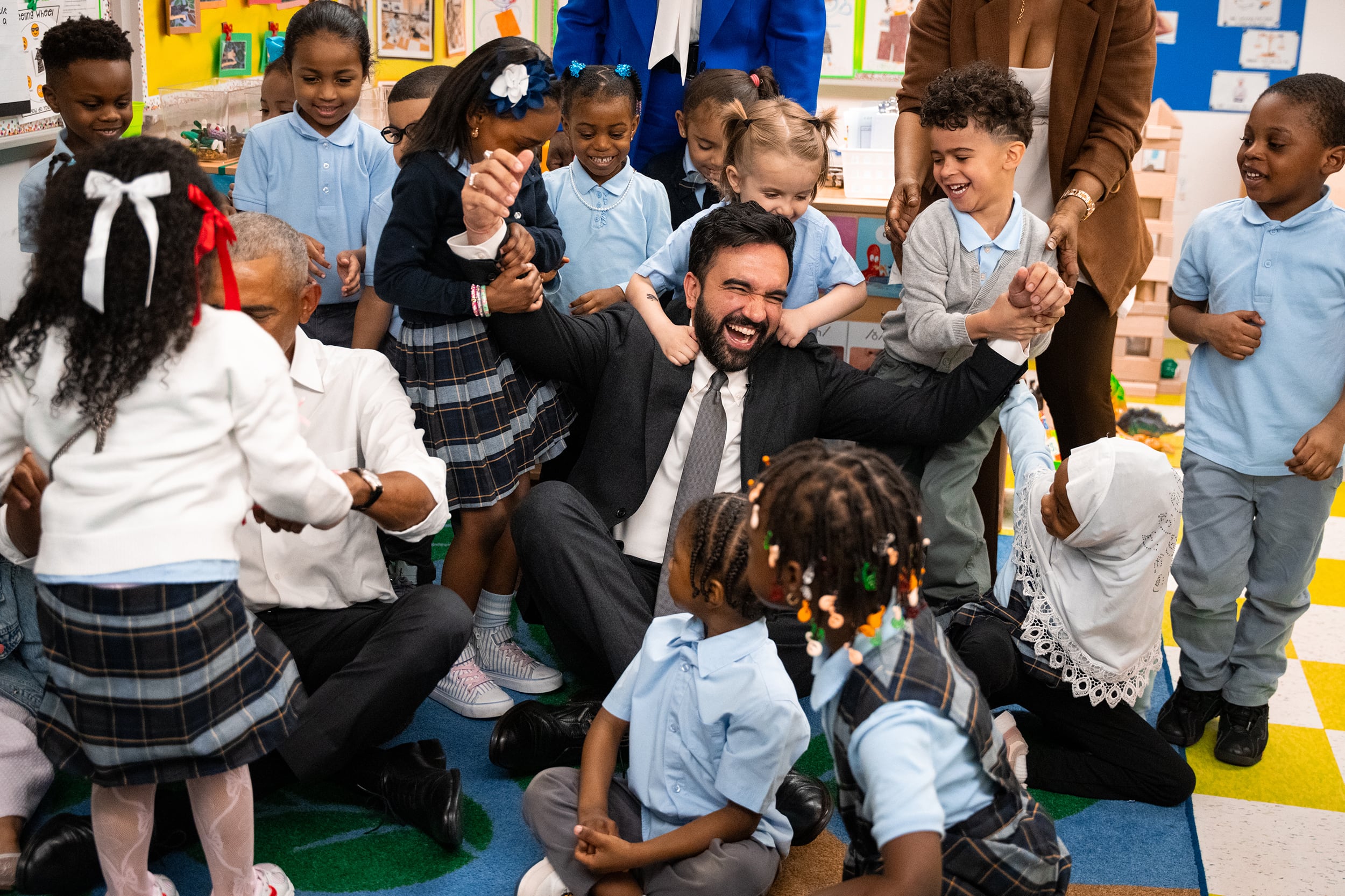 A group of preschool students swarm Mayor Mamdani with smiles in a classroom.
