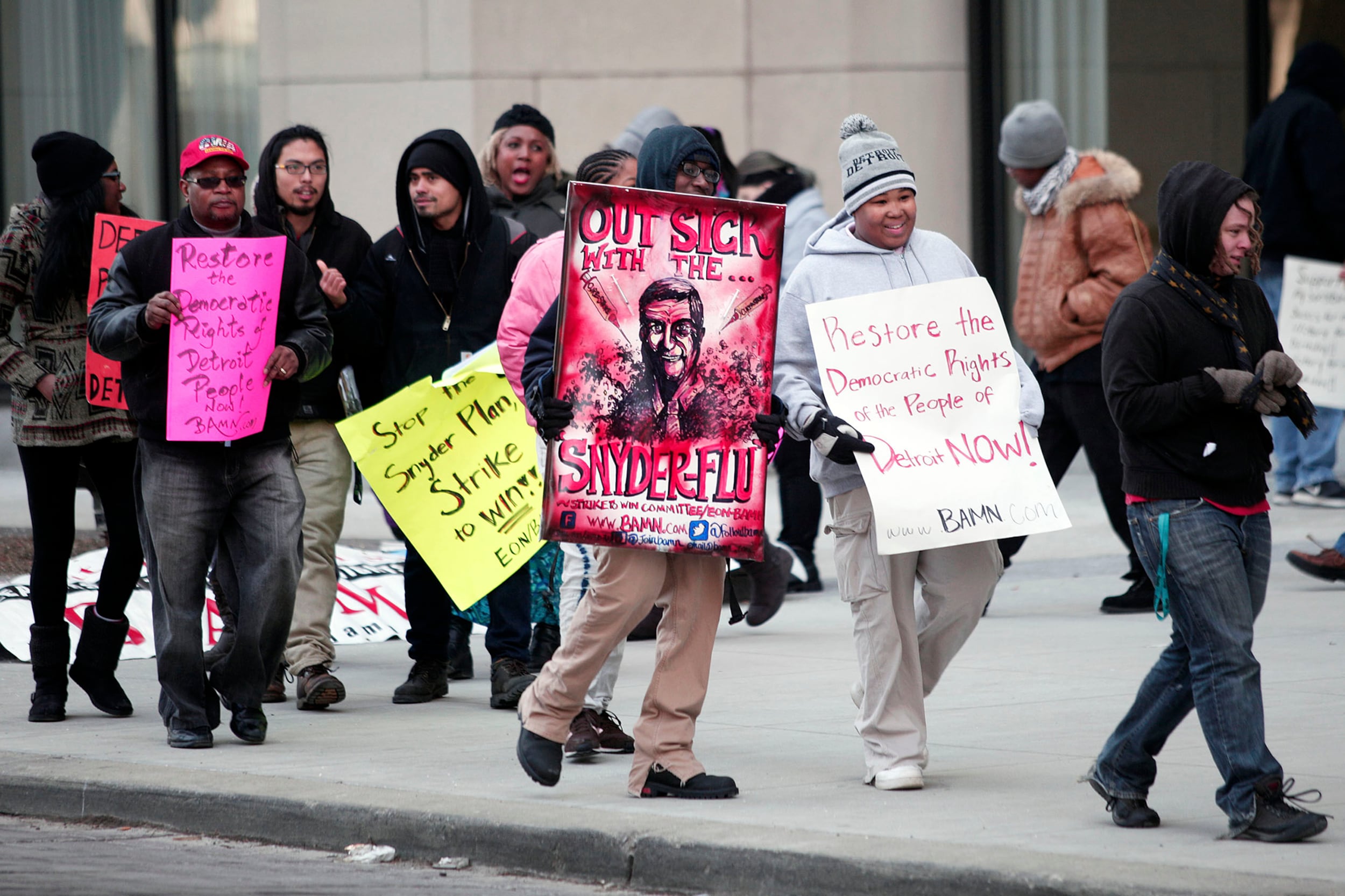 A photograph of adults with signs protesting outside of a large building.