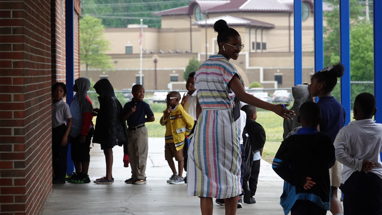 An elementary teacher walks with a student to another classroom outside.