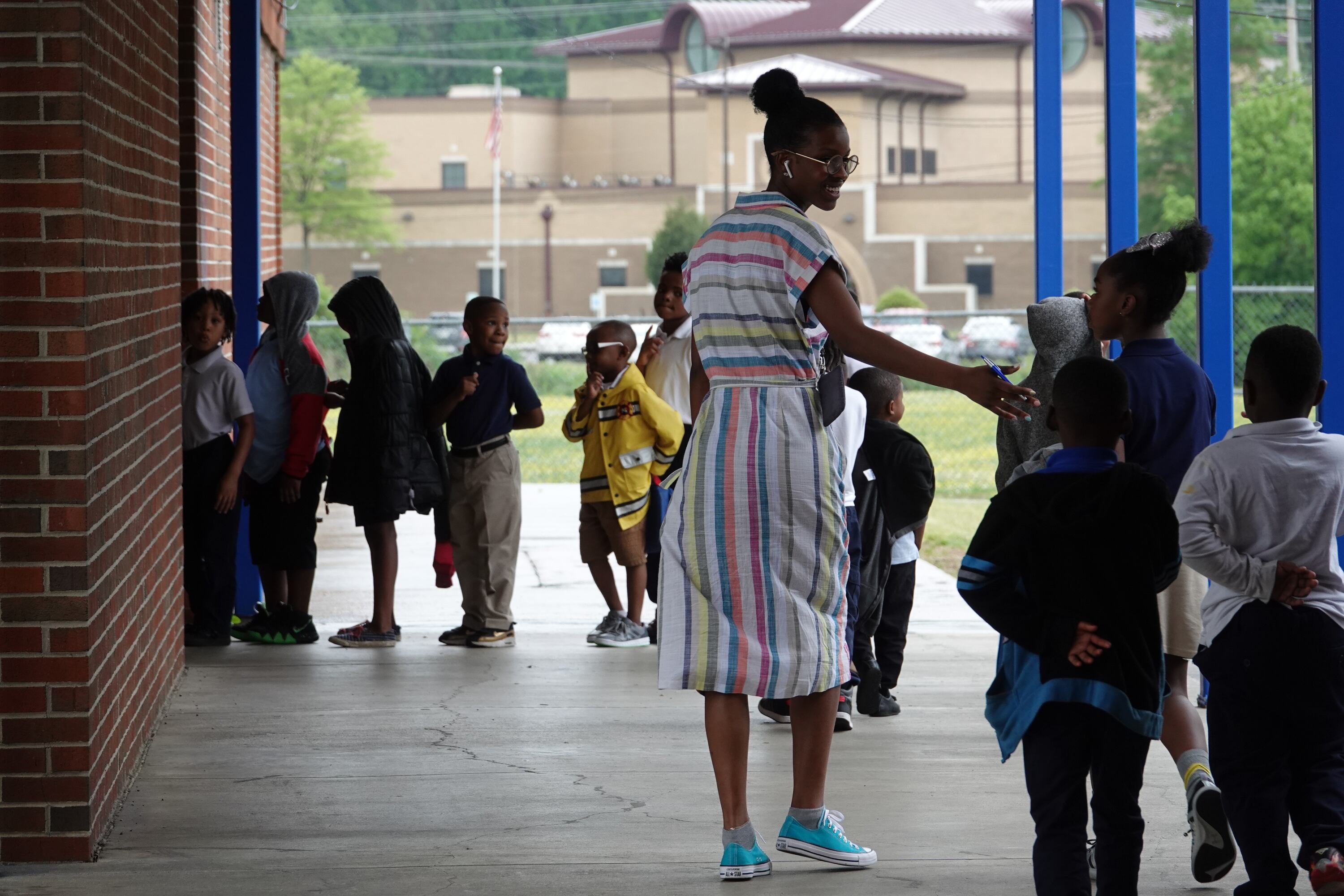 An elementary teacher walks with a student to another classroom outside.