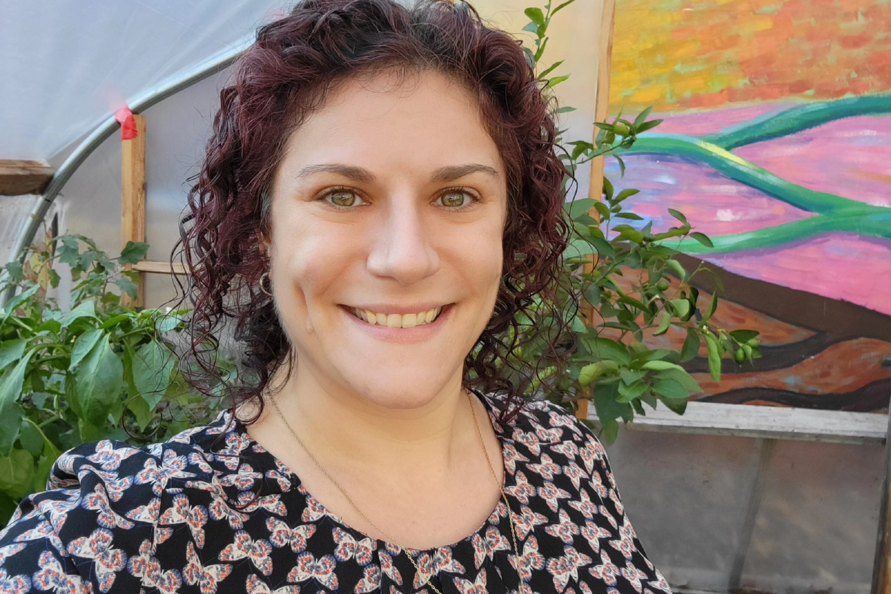A woman smiles in front of a brightly painted mural in a garden.