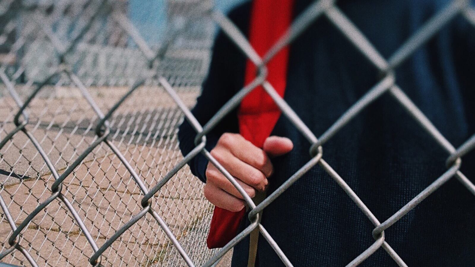 Close up of a student wearing a red backpack standing behind a wire fence.