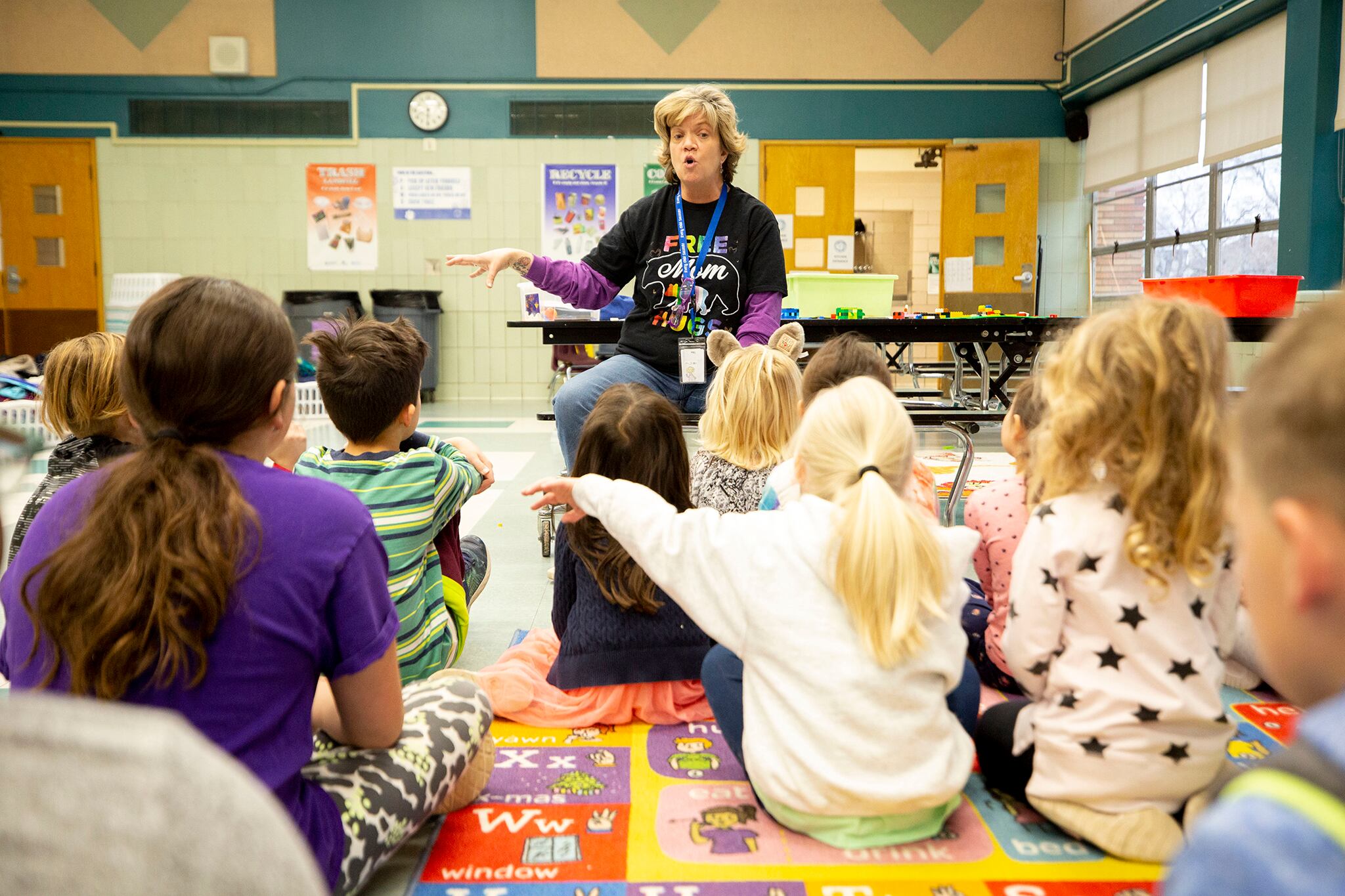 An after-school program supervisor talks to children seated on a classroom rug.
