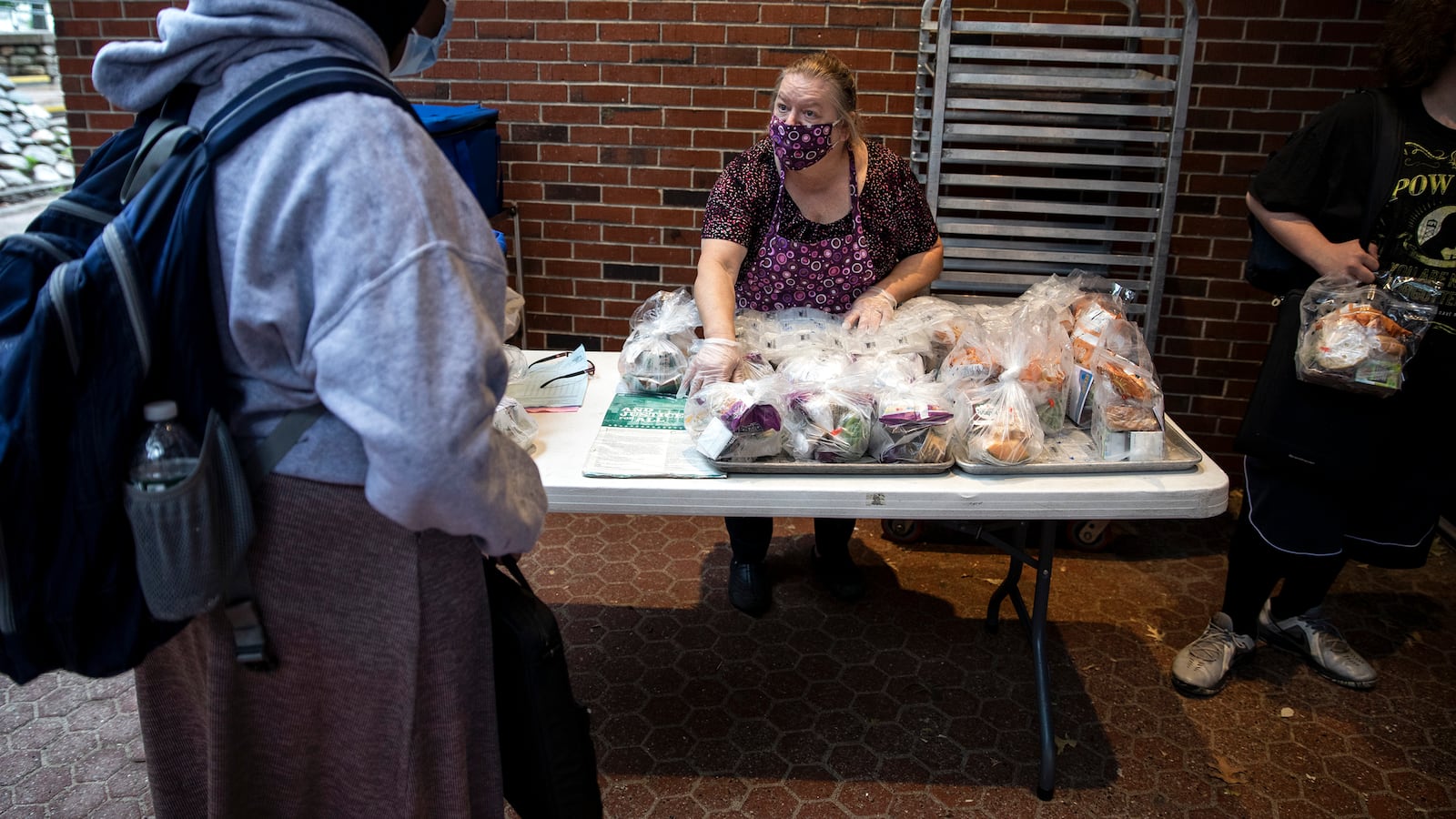 A woman wearing a mask hands food to a high school student wearing a hijab.