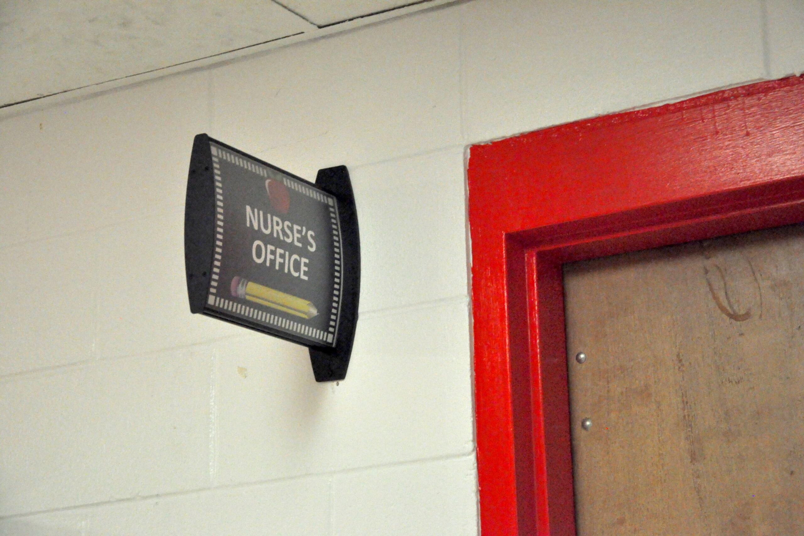 A sign in a school hallway that reads "Nurses' Office" next to a red door.